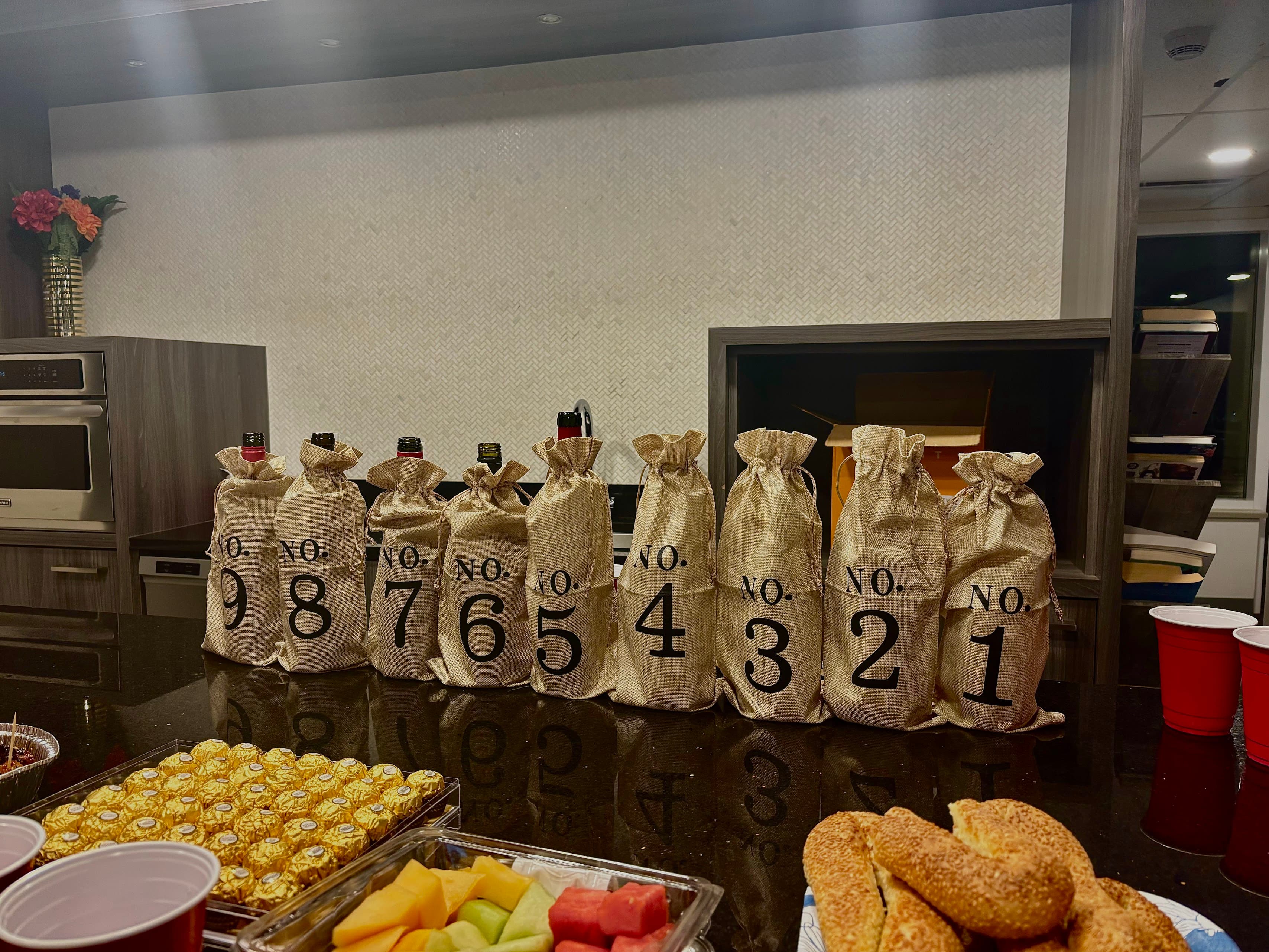 Nine wine bottles wrapped in numbered burlap bags lined up on a kitchen counter
